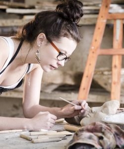 Young woman artist painting a clay face