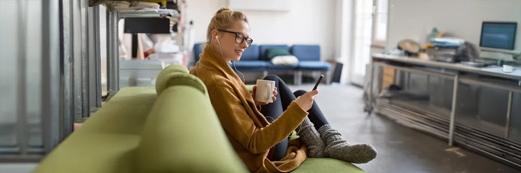 Woman sitting on her couch drinking coffee and exploring the UCHealth app.