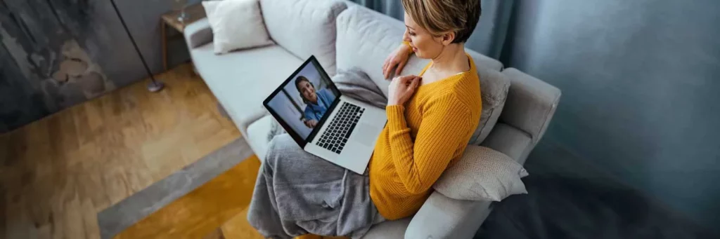 UCHealth woman on couch using virtual urgent care.