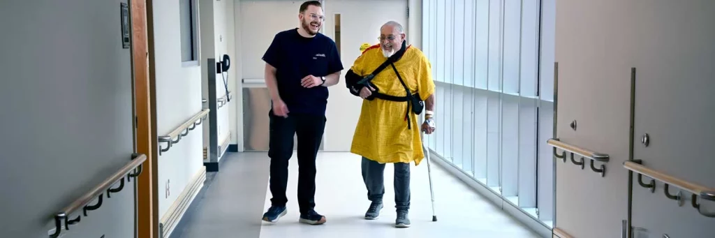UCHealth enhancing early mobility for orthopedic patients. Nurse walking patient down hallway.