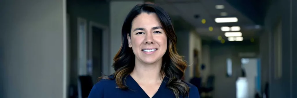 UCHealth Improving patient outcomes through sustained mobility practices. Nurse standing in hallway and smiling at camera.