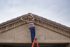 a person on a ladder hanging lights up on a house