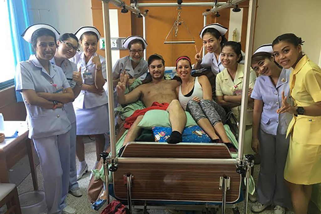 A patient and his wife pose in a hospital bed in Thailand. They are surrounded by their nurses.