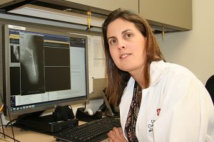 A doctor named Carla Saveli poses with an X-ray in the background.