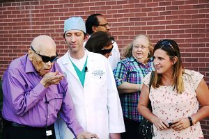 Doctors and friends watch as an older man who was blind points out objects during a short walk with his new bionic eye.