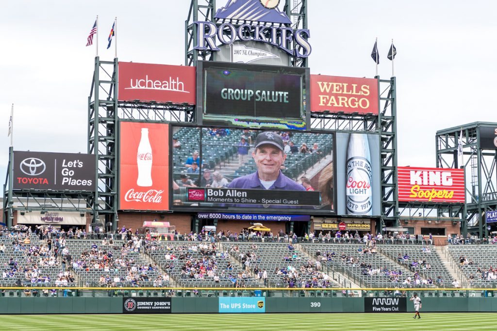 Stands at a Colorado Rockies game, a symbol of me appreciating our American way of life.