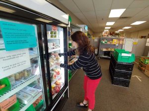 women stalks food in a food pantry in Fort Collins that addresses the whole person and is one of the ways to reduce health care costs.