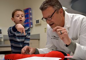 Matthew McMillan explains how his stuffed snake got injured and points out the rips in his skin as emergency physician Jamie Teumer sews up the wounds at a recent Teddy Bear Hospital event at UCHealth Poudre Valley Hospital in Fort Collins.