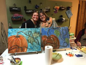 Jennifer Reid and Yvette Engel are photographed behind a craft project, including this painting project of pumpkins