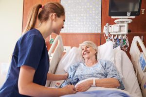 A nurse talks with a patient who is laying down in bed.