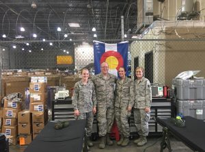 UCHealth medical relief workers wearing military fatigues gather to help in Texas after the hurricanes with a Colorado flag draped behind them.