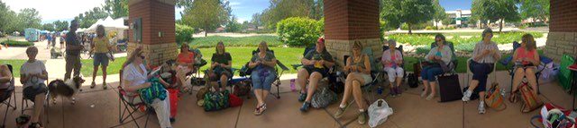 A group of people sit in lawn chairs at Fort Collins Farmers Market knitting.