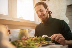 man sits at a table eating salad.