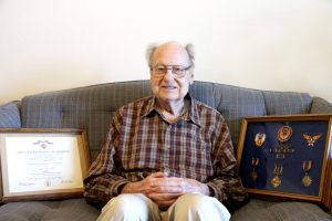 Lt. Veron Bignham sits on the couch with his framed Army Airforce awards and metals.