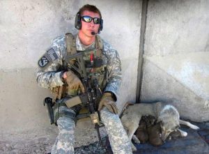 Army Sergeant Spencer Milo in Afghanistan leaning next to a wall with a dog and puppies sleeping beside him.
