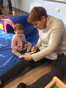 Joy, the patient, sits on the ground, reading to her granddaughter, who is about 1-year-old.