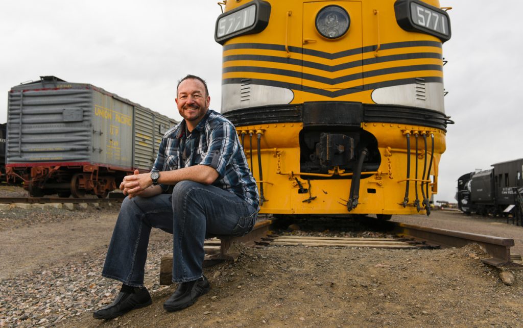 Train engineer Stephen Mullen poses in front of a yellow train. He learned he had a brain tumor that threatened his hearing.