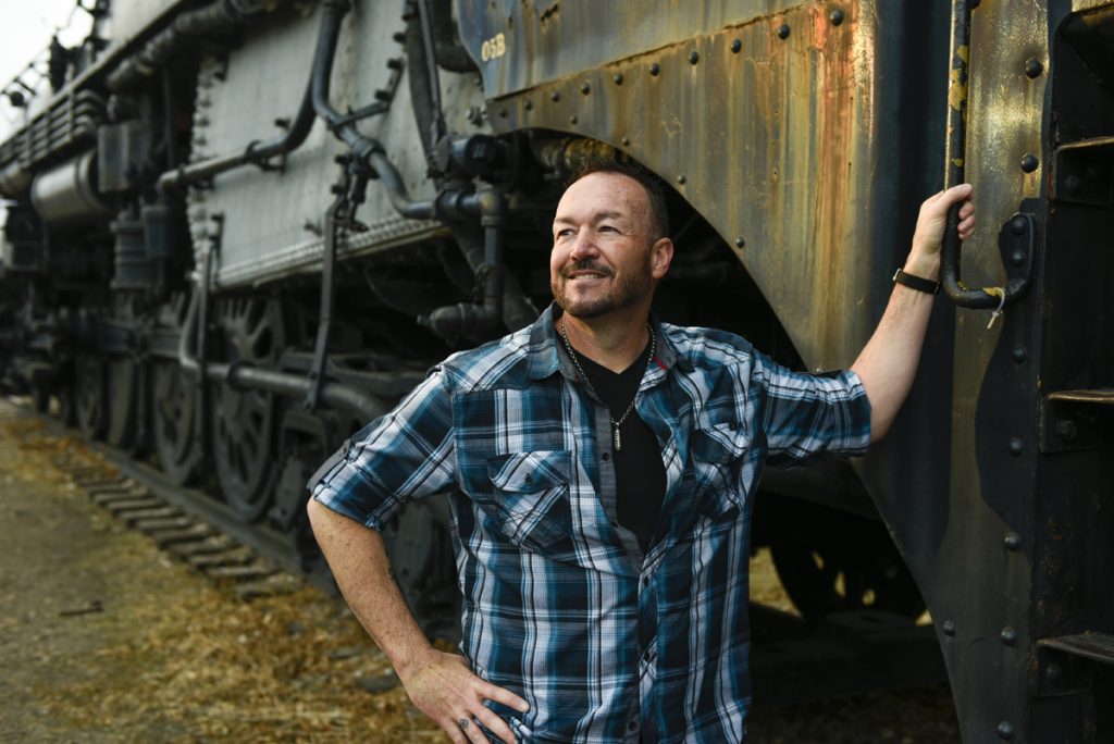 Stephen Mullen poses with a train at the Colorado Railroad Museum. Train engineer back aboard after brain tumor threatens hearing.