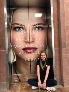 Peyton sits in front of an elevator tht shows her in her UCHealth ad.