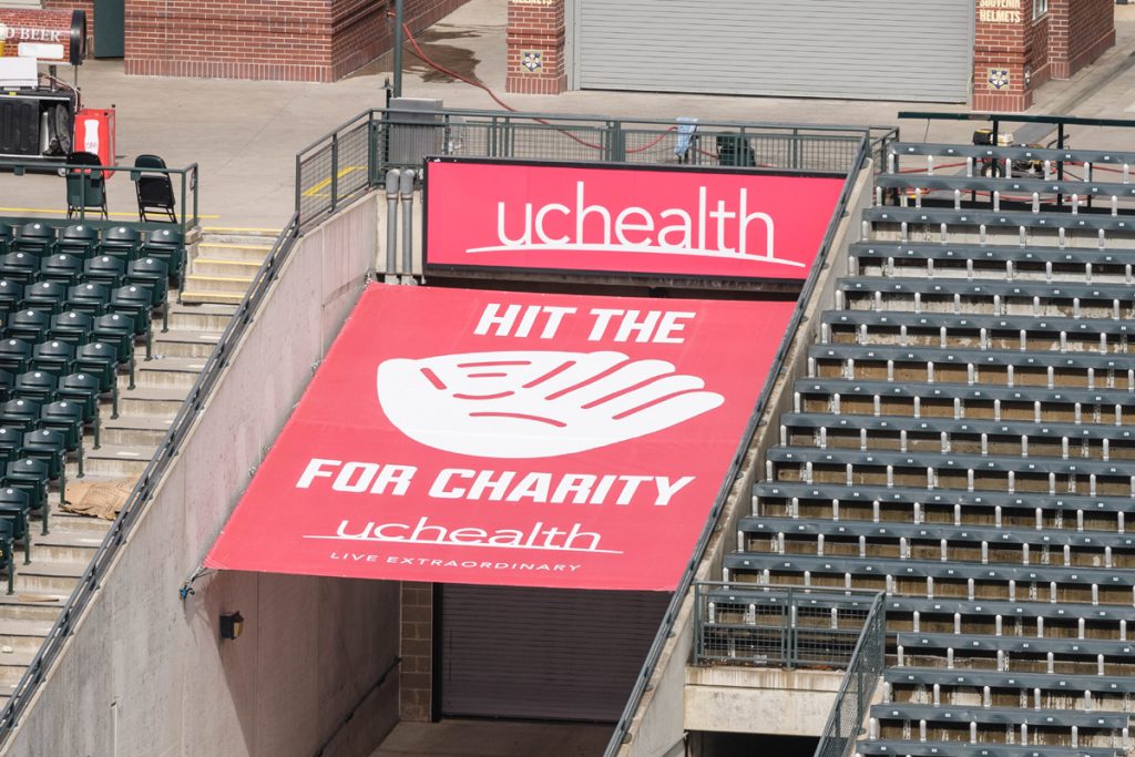 A red "Hit the Mitt" sign at Coors Field in Denver. The sign shows a big mitt with Hit the Mitt spelled out around it and UCHealth at the top. Each time a Rockies player hits a homer that strikes the sign this year, $5,000 will be donated to help with food insecurity in Colorado..