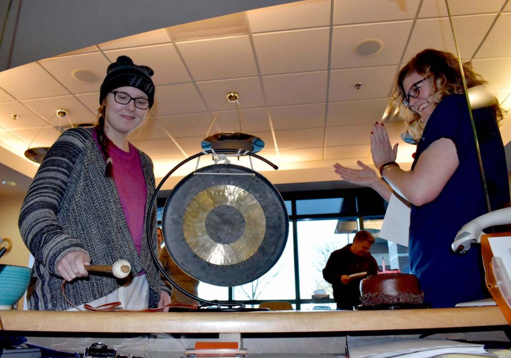 A photo of Kate Prewett banging a gong after radiation treatment.