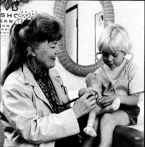 Dr. Jeanne Lewis in a 1994 photo from the Boulder Daily Camera. She's wearing a white coat and using her stethoscope to check on a young patient.