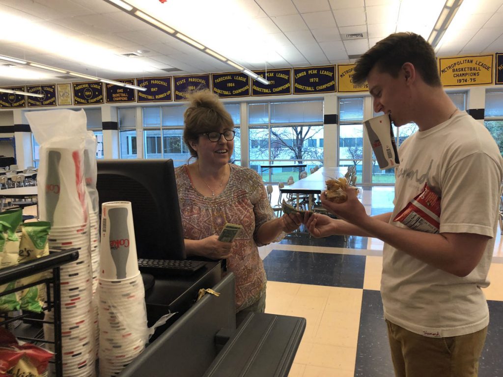 Vicki Burke stands at a cash register and collects money from a customer at Holy Family High School cafeteria.