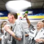 A cancer survivor laughs as she pours sparkling cider on the back of one of her supporters.