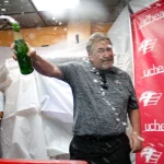 The general manager of the Colorado Eagles hockey team pops the first bottle of sparkling cider and begins to spray it on the crowd of cancer survivors and their supporters.