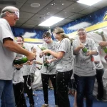 Cancer survivors and their supporters pop sparkling cider bottles and spray the cider all over each other and the Colorado Eagles locker room at a special locker room celebration for UCHealth cancer survivors.
