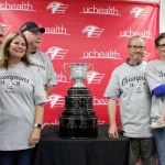 A group of people pose for a photo with the Kelly Cup.