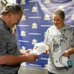The general manager of the Colorado Eagles autographs a fan’s hat at a special locker room celebration for UCHealth cancer survivors.