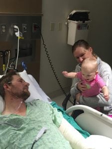 Archie Chant in his hospital bed. He's immobile as his wife and baby daughter visit him.