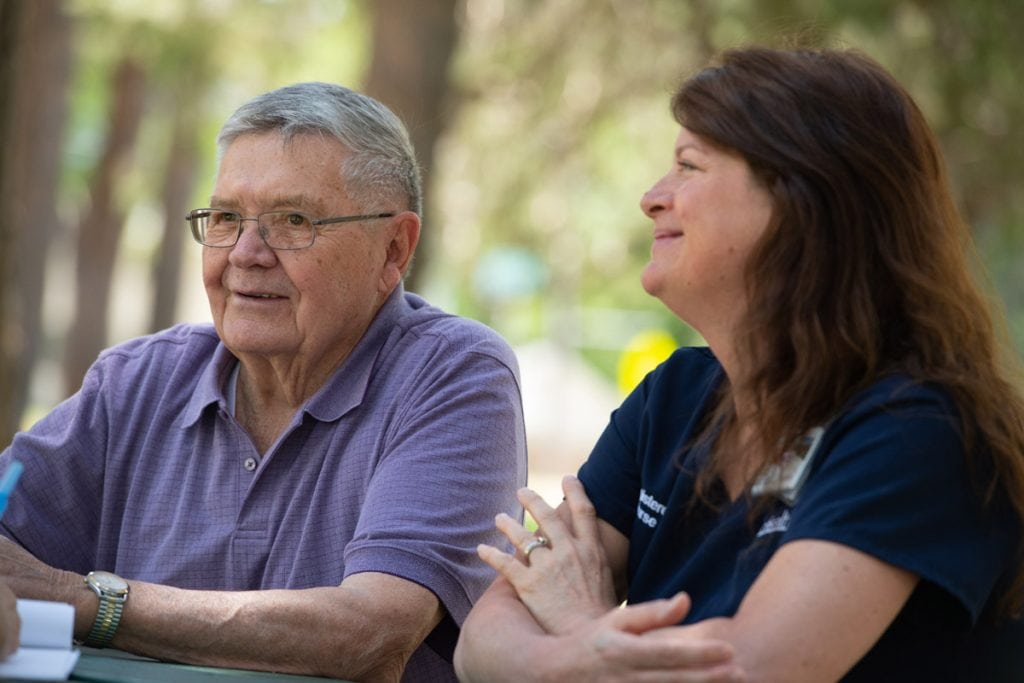 A cancer patient chats with his nurse navigator while sitting at a picnic table in a park.