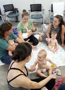 mothers and babies gather around a blanket to talk and play at a breastfeeding support group.
