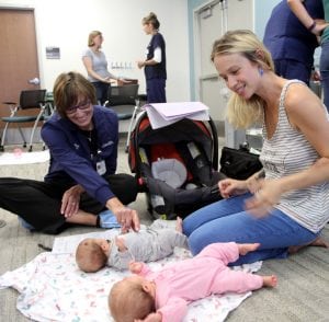 Mom smiles at twin babies on the floor.