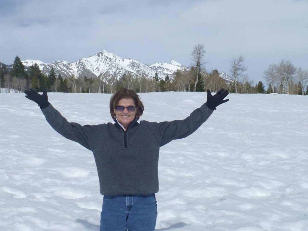 Trish Washburn holds her hands out in a snowy landscape with a mountain behind her. Washburn is passionate about skiing. Thanks to help from a psychologsit at the UCHealth primary care clinic close to her home, she's regaining her confidence on the slopes. Photo courtesy of Trisha Washburn.