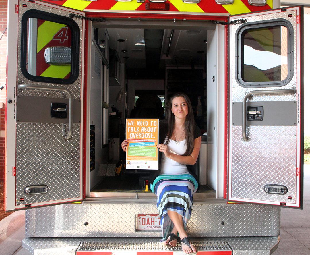Gina Zappia sits on back of ambulance with event sign.