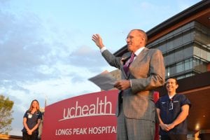 Hospital president stands in front of facility on opening day and gestures to crowd gathered.