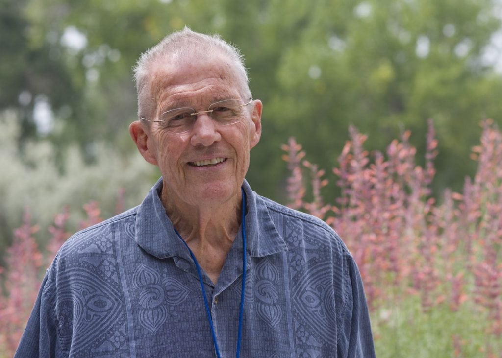 Portrait of Bill Brennan who has achieved a new lease on life after CAR-T immuontherapy treatment for blood cancer. He poses with some flowers behind him.