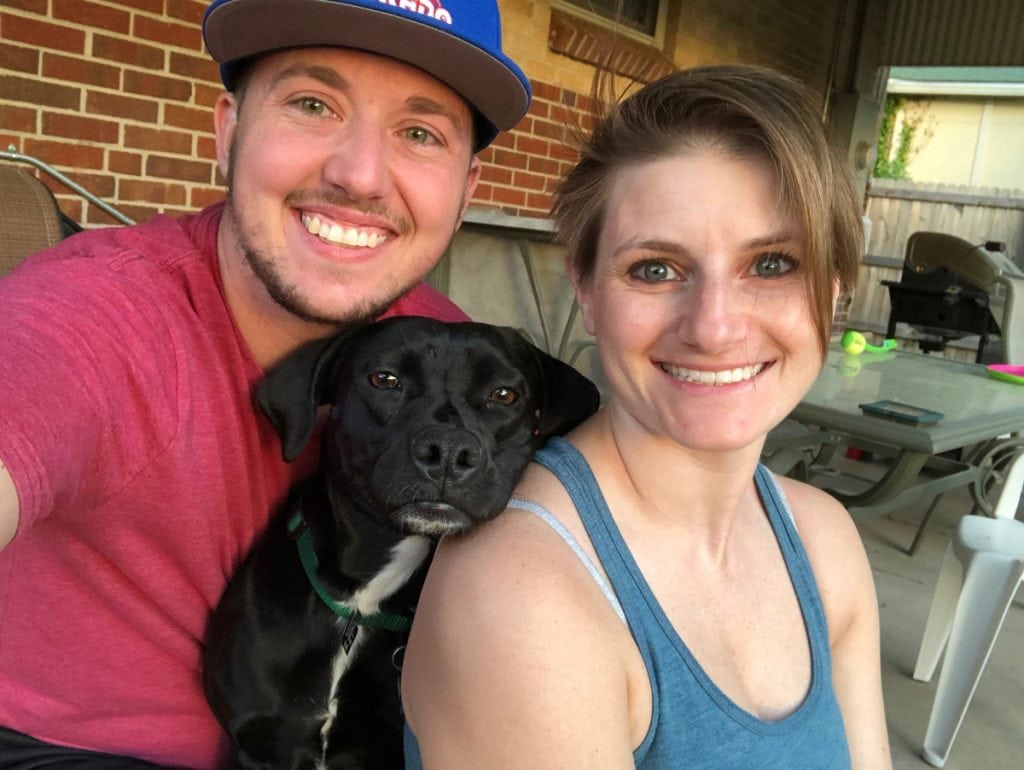 A couple poses with their dog in the middle.