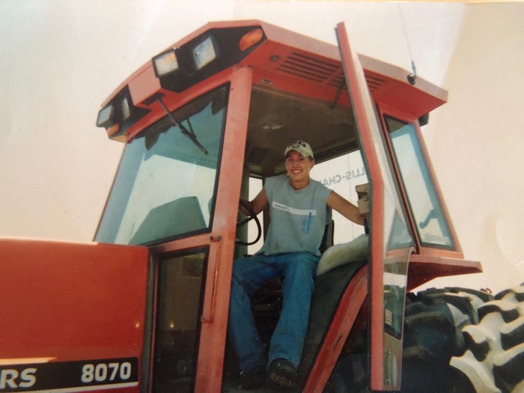 A teen sits in the cab of a large orange tractor. Mal Foust looks male and wears a ball cap, jeans and T-shirt. But he had been born a girl.