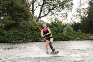 A woman wakeboards. Her left leg is amputated and she wears a prosthetic.