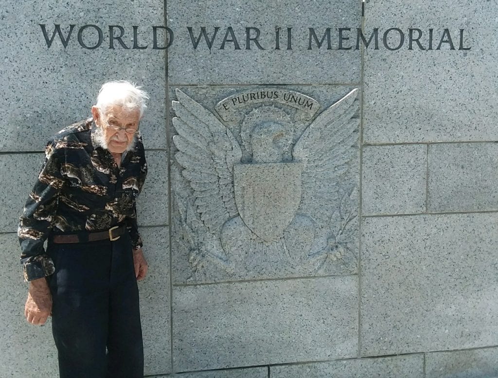 A 94-year-old WW II veteran, Virgil Hughes, poses with a sign that says World War II Memorial. He visited the memorial in Washington, D.C. in May.