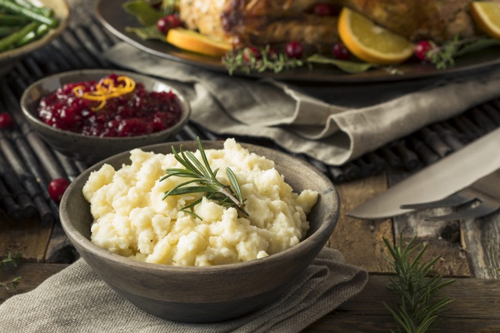 mashed potatoes with a sprig of rosemary on top and cranberries and turkey visible in the bakcground