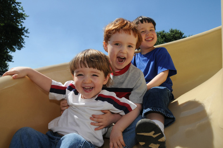 3 boys smiling as they come down a slide