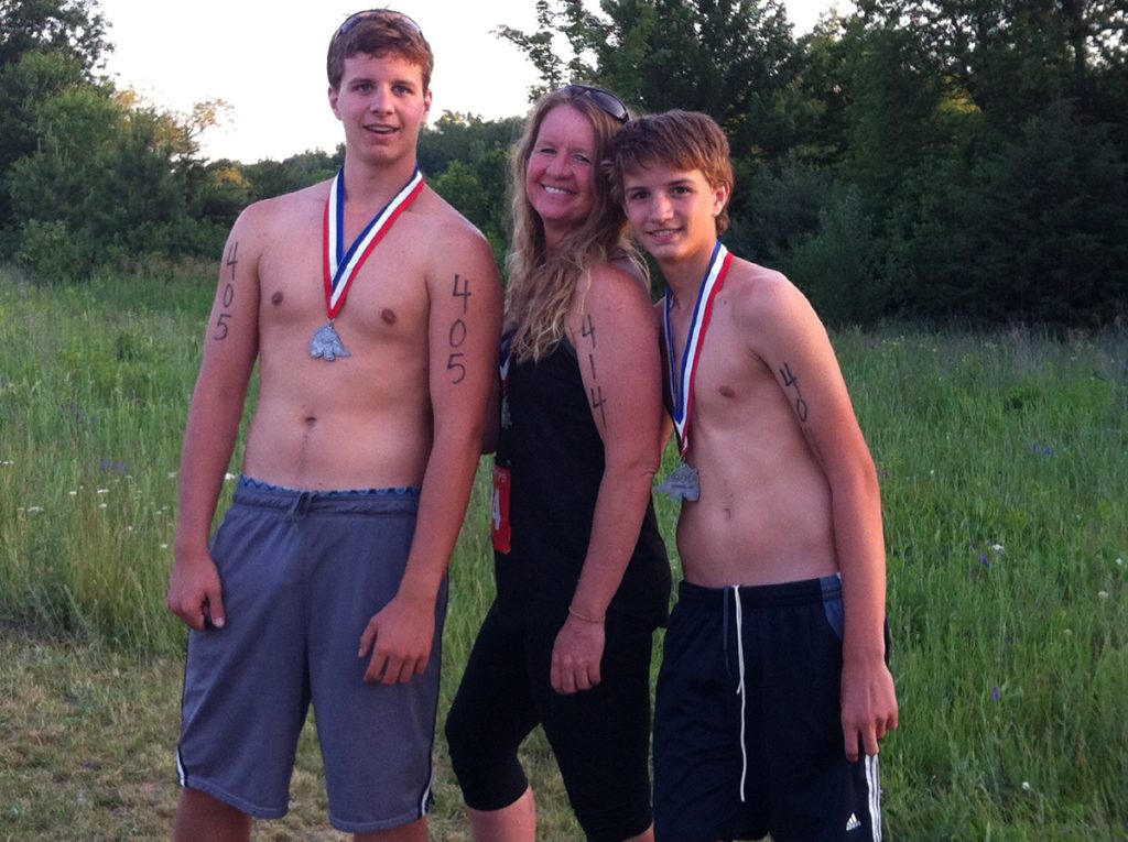 Dr. Heather Holmstrom poses with her two sons at a triathalon. All three are wearing medals and they are posing outside after the race.