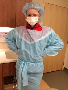 A teenage boy is dressed in scrubs and a mask. He's practicing to clean out his mom's wound after she suffered a bad hockey injury.