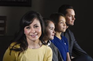 Portrait of mom who savd her family from carbon monoxide poisoning with her two kids and husband in the background.