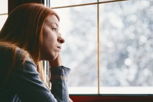 A sad woman looks out the window on a winter day.